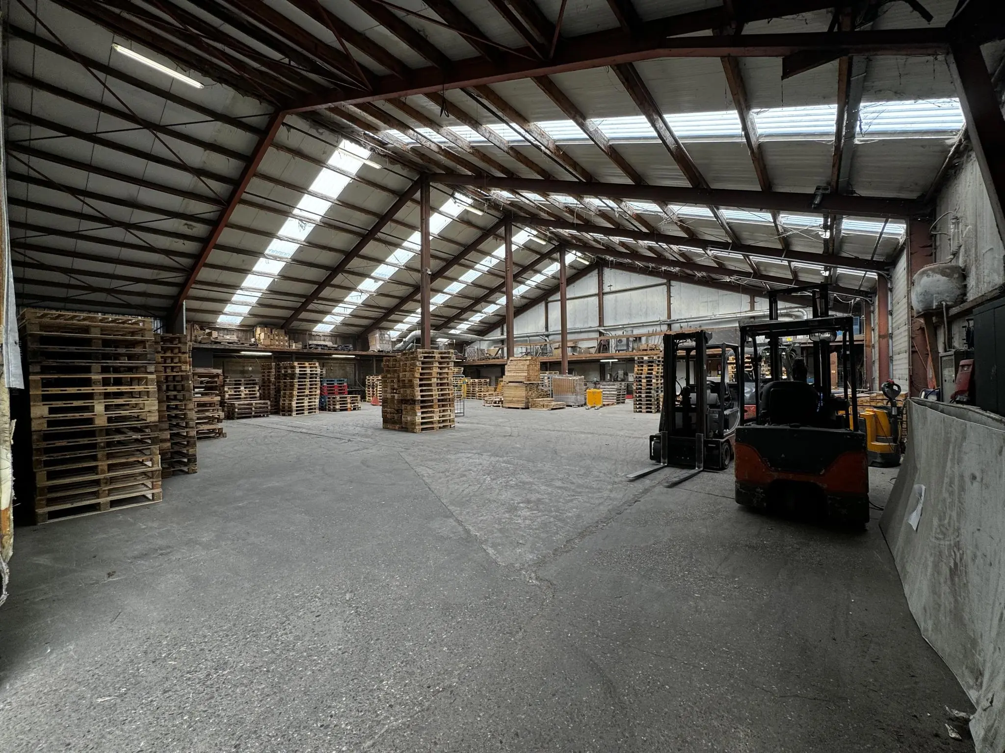 Interieur van een ruim magazijn aan de Graaf van Lynden van Sandenburgweg met stapels houten pallets en heftrucks.